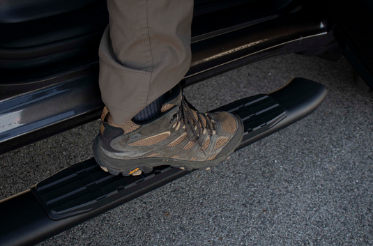 Alt text: "Person stepping on a Fishbone Offroad 5-Inch Oval Side Step installed on a 2019-Current Ram 1500 Quad Cab."