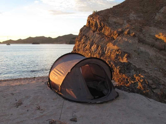"Front Runner Flip Pop Tent set up on a beach at sunset with calm sea and mountains in the background."