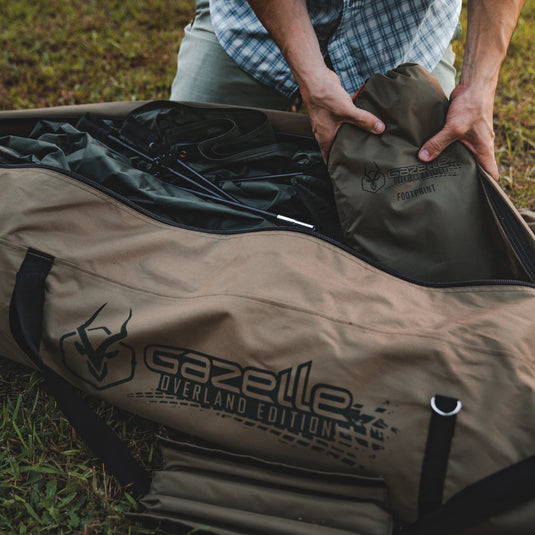 Person packing a Gazelle Tents T4 Hub Tent Overland Edition with footprint into a carry bag on grass.