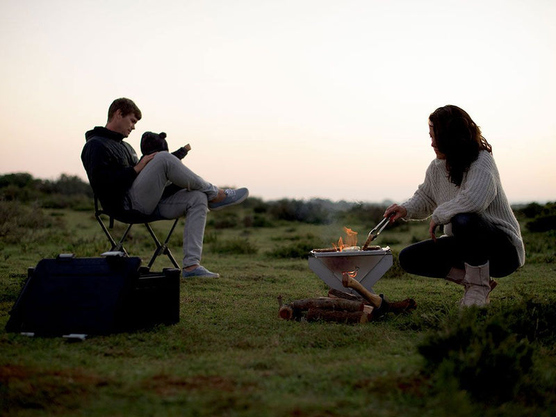 Load image into Gallery viewer, Two people relaxing by a portable Front Runner BBQ/Fire Pit during a twilight outdoor adventure.
