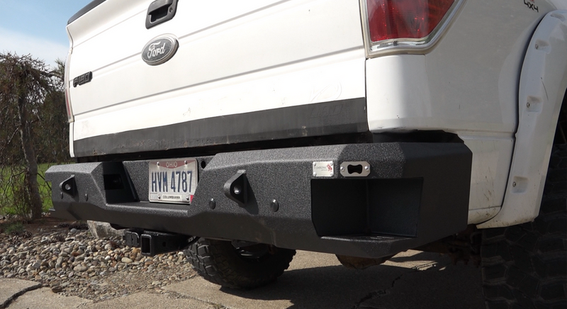 Load image into Gallery viewer, Alt text: &quot;Fishbone Offroad rear step bumper installed on a 2009-2014 white Ford F-150, showcasing rugged design and integrated steps.&quot;
