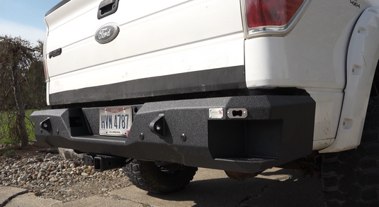 Alt text: "Fishbone Offroad rear step bumper installed on a 2009-2014 white Ford F-150, showcasing rugged design and integrated steps."