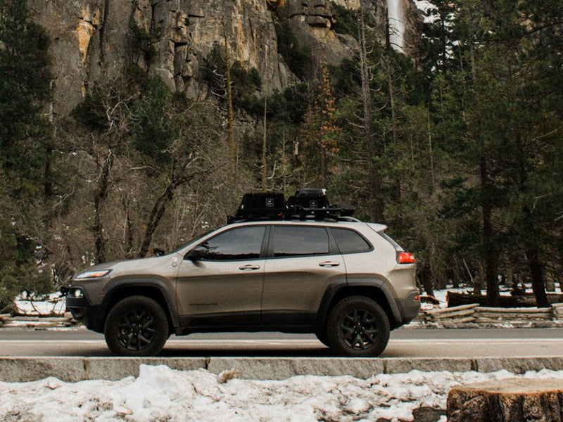 Load image into Gallery viewer, Jeep Cherokee KL with Front Runner Slimline II Roof Rail Rack Kit against a backdrop of snowy mountains and forest.
