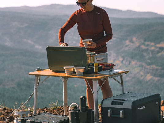 Person using Front Runner Dometic Go Compact Camp Table with bamboo surface during outdoor camping adventure.