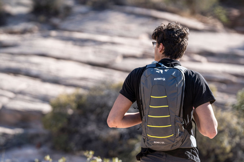 Load image into Gallery viewer, Man hiking with Klymit Echo 12L Hydration Pack in outdoor setting
