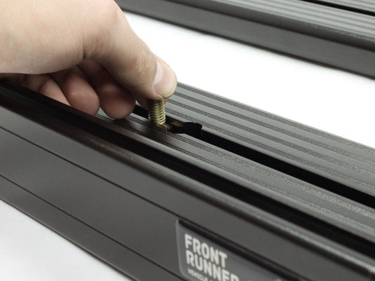 Close-up of a hand installing a component on the Front Runner Slimline II Load Bed Rack Kit for a Dodge RAM Mega Cab 2-Door Pickup Truck, model years 2002-2008.