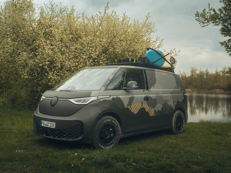 Load image into Gallery viewer, Volkswagen ID Buzz equipped with Front Runner Slimline II Roof Rack Kit holding a surfboard on a scenic lakeside background.

