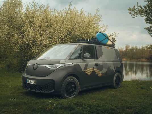 Volkswagen ID Buzz equipped with Front Runner Slimline II Roof Rack Kit holding a surfboard on a scenic lakeside background.
