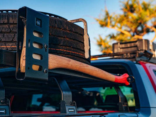 Front Runner Axe Bracket securely mounted on vehicle roof rack holding an axe with wooden handle and red head, outdoor adventure gear