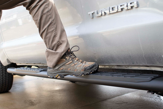 Person stepping onto a black 5-inch oval Fishbone Offroad side step on a Toyota Tundra Crew Max Cab.