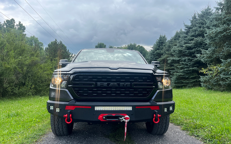 Load image into Gallery viewer, Alt text: Black 2019-2023 Ram truck with Fishbone Offroad Pike Front Bumper featuring LED lights and red tow hooks.
