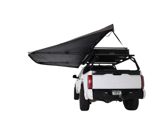 Alt text: inchWhite pickup truck with a Freespirit Recreation 180 Degree Awning fully extended, mounted on a roof rack, providing shade and shelter.inch