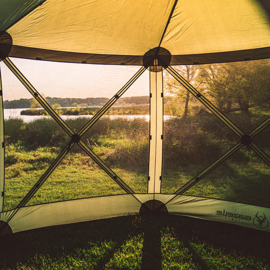 Interior view of a Gazelle Tents G6 6-Sided Portable Gazebo set by a lakeside at sunset with wind panels attached.