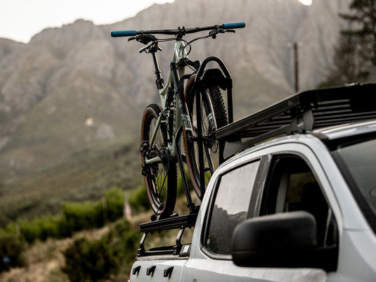 Front Runner Pro Bike Carrier mounted on vehicle roof with mountain bike in scenic outdoor setting