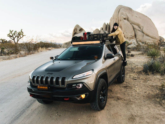 Jeep Cherokee KL with Front Runner Slimline II Roof Rail Rack Kit_installed in a desert landscape setting, person loading gear onto roof rack.