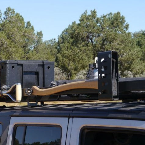 Front Runner Axe Bracket mounted on vehicle roof rack holding an axe outdoors