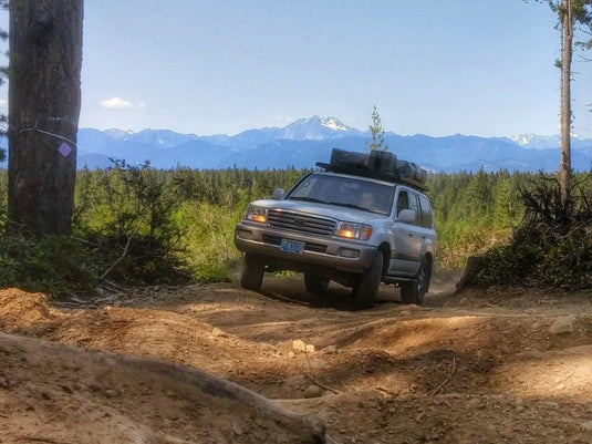 Front Runner Toyota 100 Series Land Cruiser with Slimline II Roof Rack Kit on off-road trail in forested mountainscape