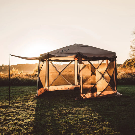 Gazelle Tents G6 Deluxe 6-Sided Portable Gazebo set up in grassy field during sunset.