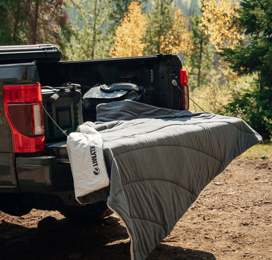 Klymit Horizon Overland Portable Blanket spread in truck bed outdoors with forest in background