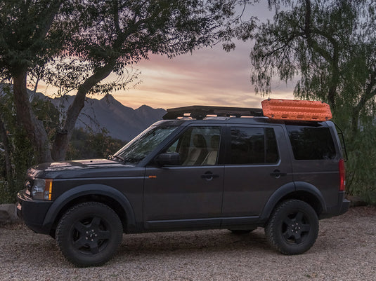 Dark SUV equipped with Front Runner Recovery Device and Gear Holding Side Brackets mounted on roof rack at dusk with mountains in the background
