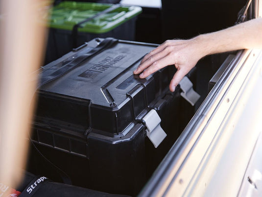 Alt text: "Person placing a Front Runner Wolf Pack Pro Hi-Lid storage box in the back of a vehicle."