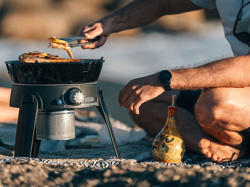 Load image into Gallery viewer, Person grilling on a portable Cadac Safari Chef 30 HP gas barbeque while camping, showcasing the ease and convenience of the 5-piece camp cooker set.
