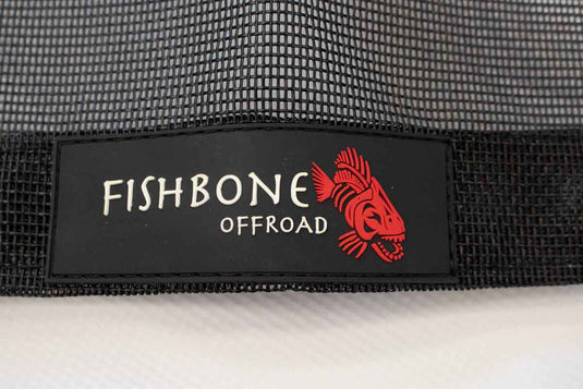 Alt text: "Close-up of the Fishbone Offroad brand logo on a 2020-Current Jeep Gladiator JT Rear Sun Shade with mesh fabric background."