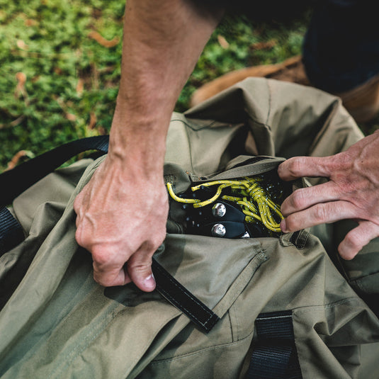 Person packing yellow rope and metallic gear into a water-resistant Gazelle Tents T3 Tandem Duffle Bag outdoors.