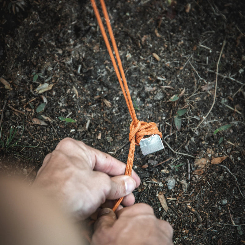 Load image into Gallery viewer, Close-up of a person tying a secure knot on an orange tent rope, a detail of the Gazelle Tents T8 Hub Tent setup process.
