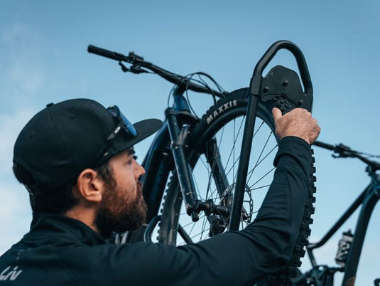 Man securing a bicycle onto the Front Runner Pro Bike Carrier mounted on a vehicle.