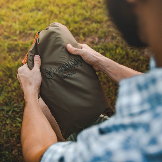 Person holding a folded Gazelle Tents T4 Hub Tent Overland Edition in a carrying case with footprint logo outdoors