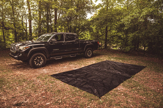 Gazelle Tents T4 Plus & T8 Footprint ground sheet laid out on forest floor next to a black pickup truck for outdoor camping setup.
