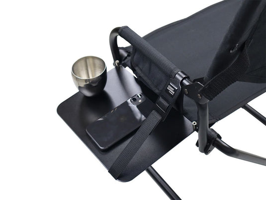 Alt text: "Front Runner Expander Chair with attached side table holding a metal cup and smartphone, showcasing the convenience and portability of the camp chair accessory."