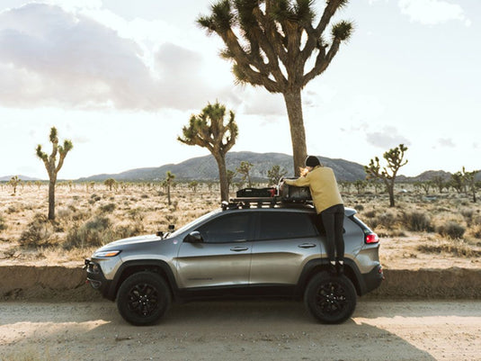 Person using Front Runner Jeep Cherokee KL Slimline II Roof Rail Rack Kit in a desert landscape.