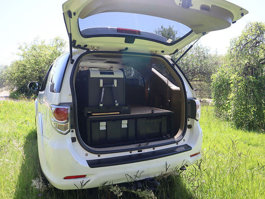 Alt text: "Front Runner 4 Wolf Pack Pro Storage System Kit installed in the trunk of a vehicle, showcasing space-saving and organizational features in a natural outdoor setting."