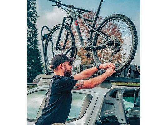 Man securing mountain bike onto Front Runner Pro Bike Carrier on vehicle roof