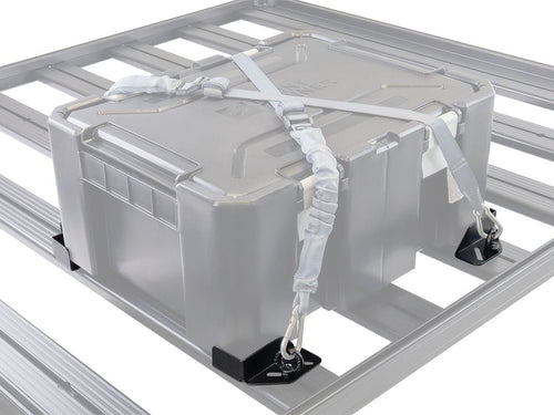 Alt text: inchFront Runner Adjustable Rack Cargo Chocks securing a grey storage box on a vehicle roof rack with straps and metal clasps.inch