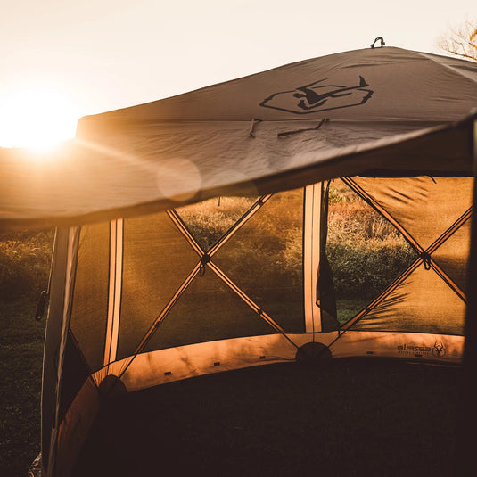 Gazelle Tents G6 Deluxe 6-Sided Portable Gazebo set up outdoors with sun setting in the background, highlighting its spacious design and durable frame.