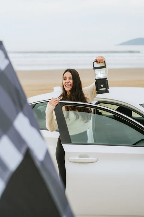 Load image into Gallery viewer, Woman holding Freespirit Recreation ReadyLight camp lantern at beachside with car.

