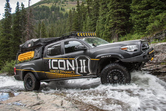 ICON Vehicle Dynamics Alpha truck with Black Ring wheels crossing a river in a forest setting.