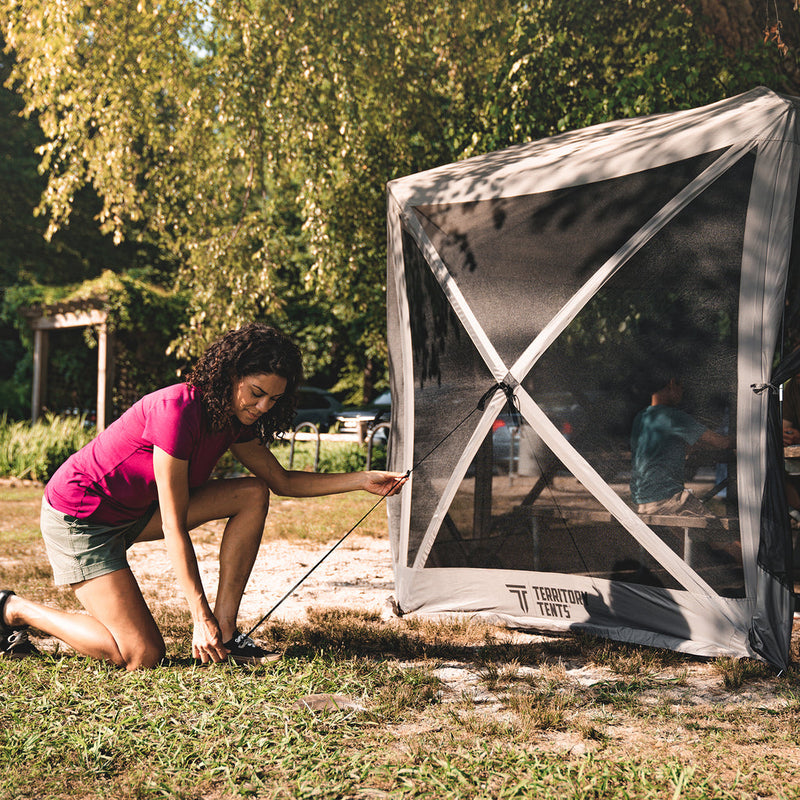 Load image into Gallery viewer, Alt text: &quot;Woman setting up a Territory Tents 6-Sided Screen Tent outdoors on grass with trees in the background.&quot;
