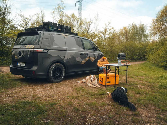 "Volkswagen ID Buzz equipped with Front Runner Slimline II Roof Rack parked outdoors with camping gear, person, and dogs"