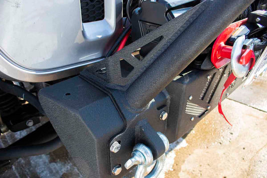 Alt text: "Close-up view of black Fishbone Offroad Barracuda Modular Bumper installed on a Jeep Wrangler with visible D-ring and winch details."