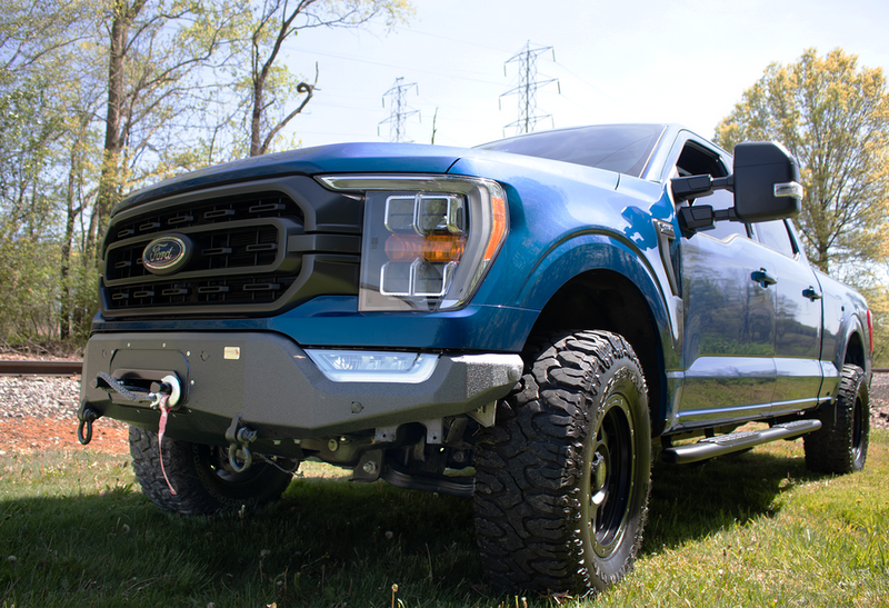 Load image into Gallery viewer, Blue Ford F-150 truck with Fishbone Offroad winch plate on Pelican front bumper, showcased outdoors.
