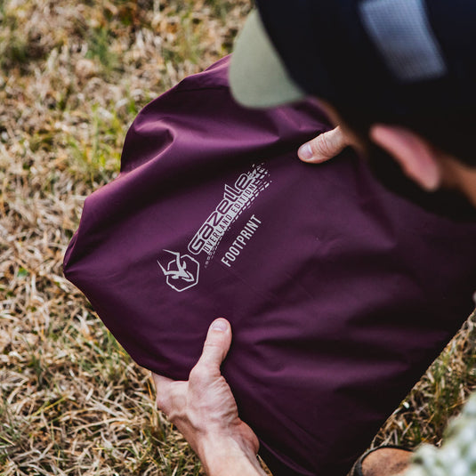 Person unpacking Gazelle Tents T-Hex Hub Tent Overland Edition footprint on grassy terrain.