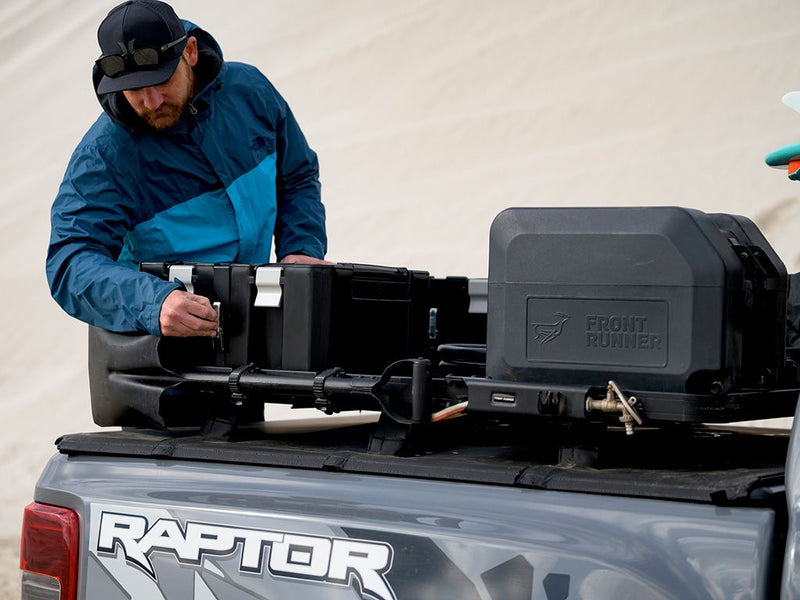 Load image into Gallery viewer, Man installing Front Runner Wolf Pack Pro rack mounting brackets on a pickup truck bed.

