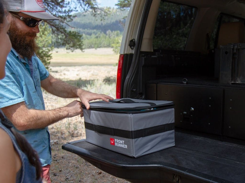 Load image into Gallery viewer, Man placing a Front Runner Flat Pack storage bag in the trunk of an SUV for an outdoor adventure.
