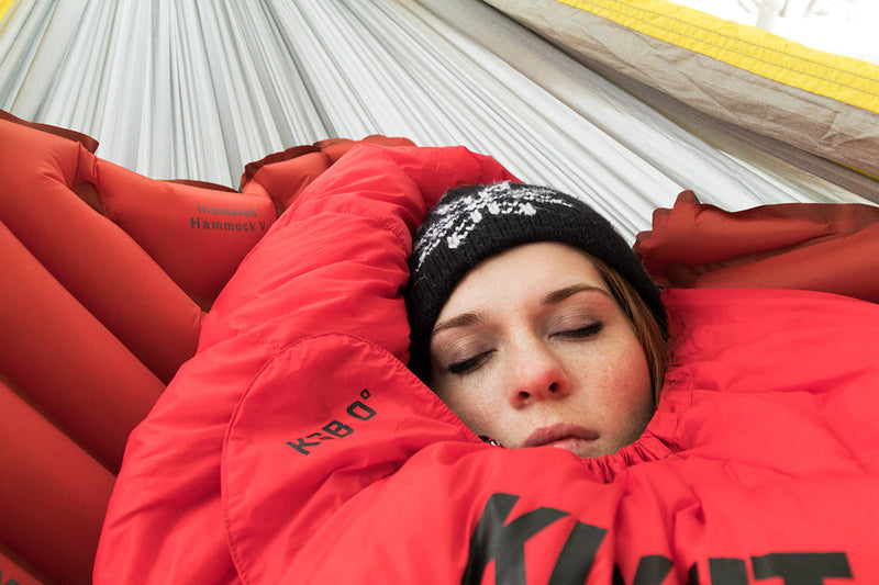 Load image into Gallery viewer, Woman resting on a Klymit Insulated Hammock V Sleeping Pad in a hammock with a warm beanie
