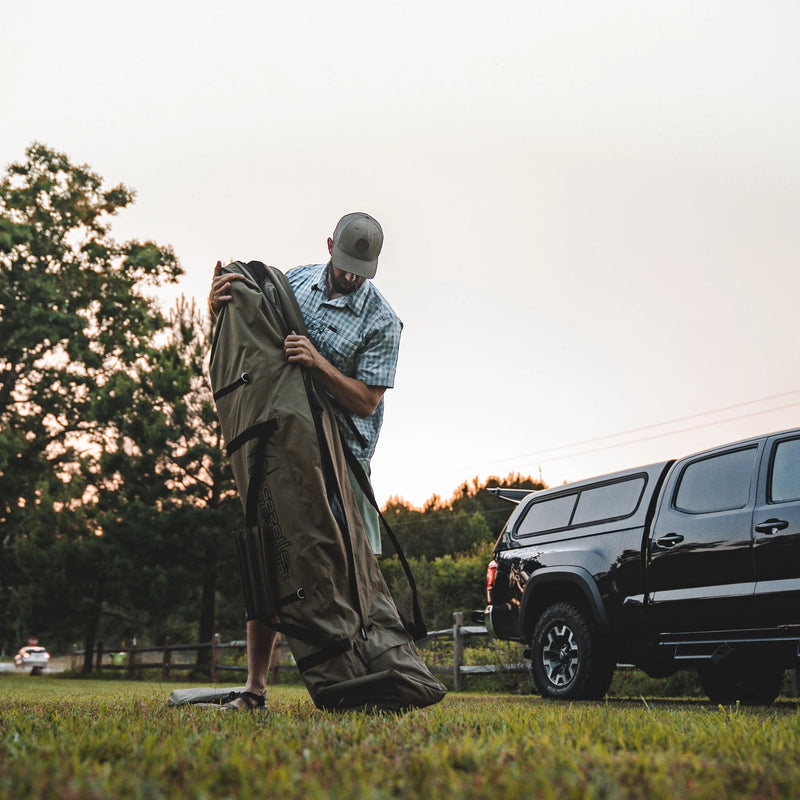 Load image into Gallery viewer, Man unpacking Gazelle Tents T4 Hub Tent Overland Edition from carrier bag near SUV at dusk.
