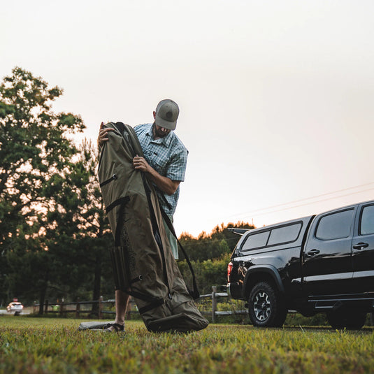 Man unpacking Gazelle Tents T4 Hub Tent Overland Edition from carrier bag near SUV at dusk.